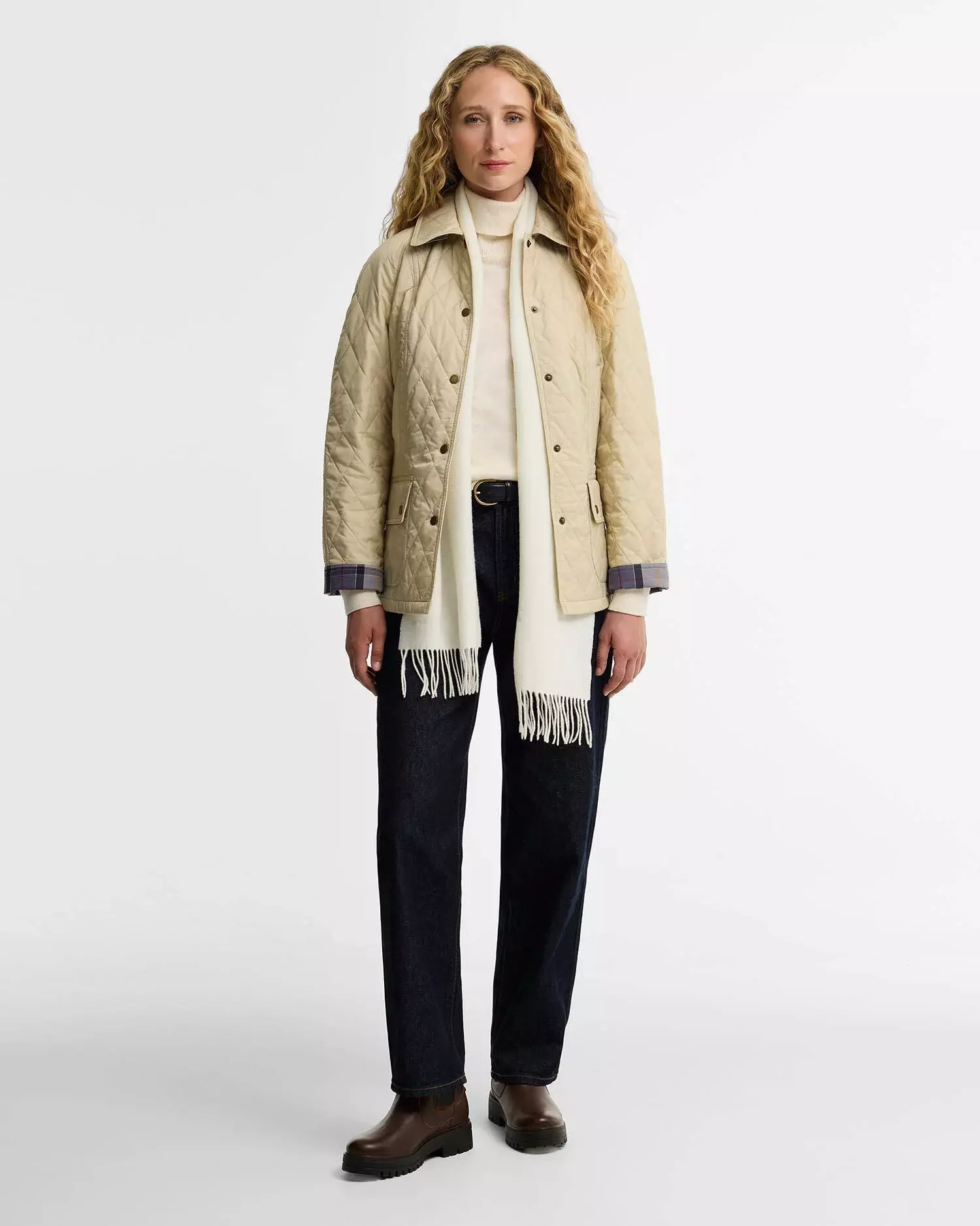 Woman styling brown chelsea boots with dark jeans an ivory turtleneck and a beige quilted jacket