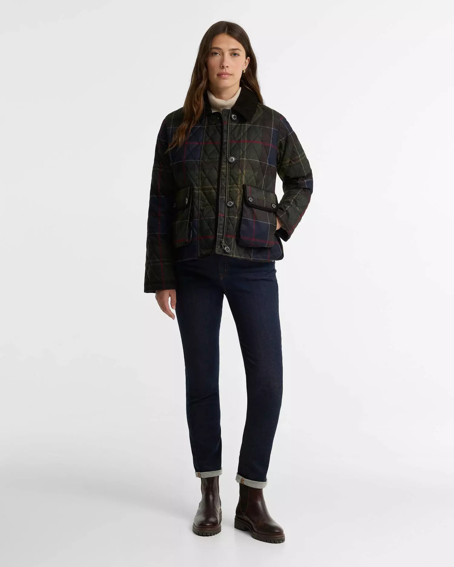 Woman in green plaid quilted jacket, cream turtleneck, dark cuffed jeans, and brown Chelsea boots
