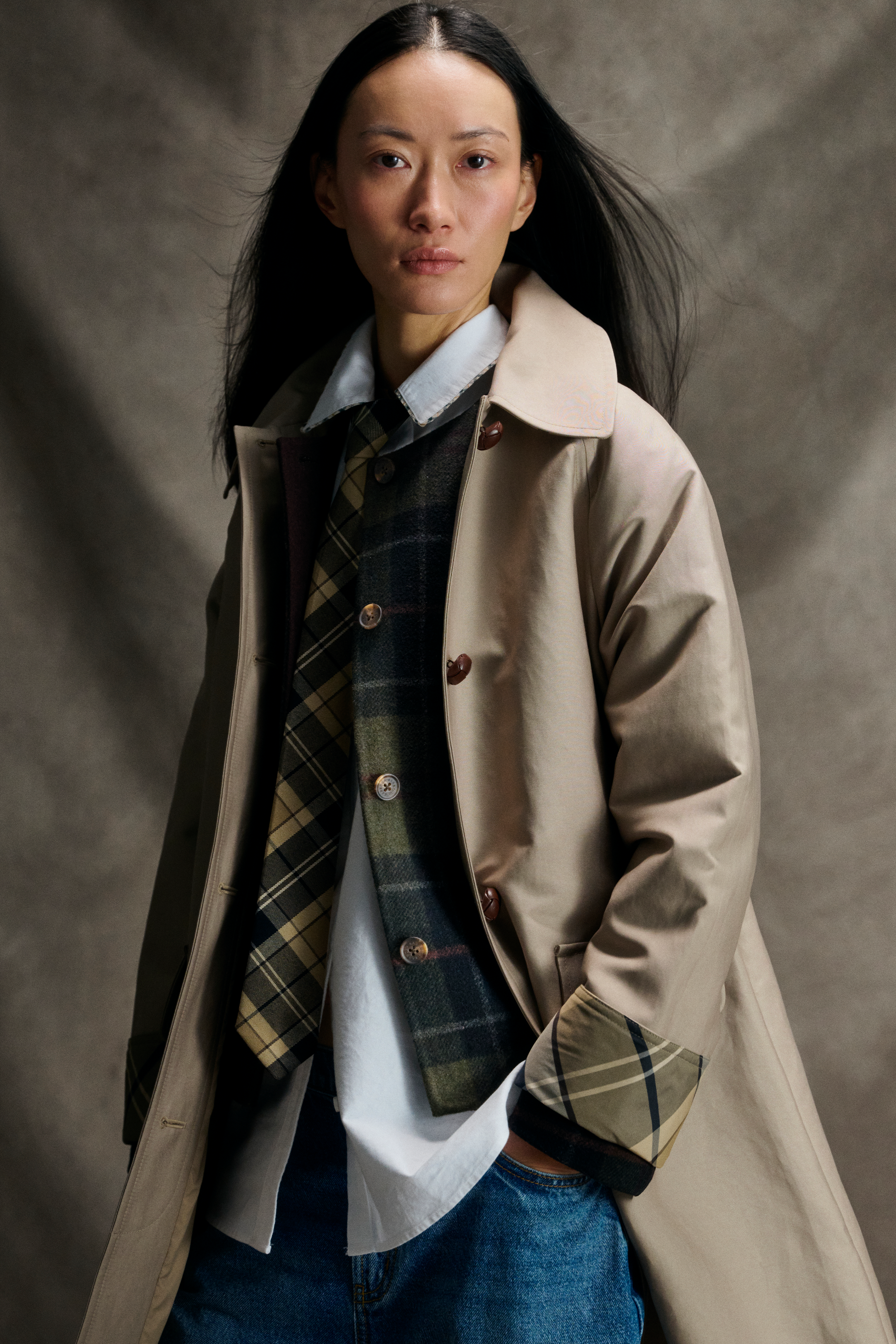 Woman in a beige trench coat with plaid lining, white shirt, green plaid vest and tie, for womens coat styles