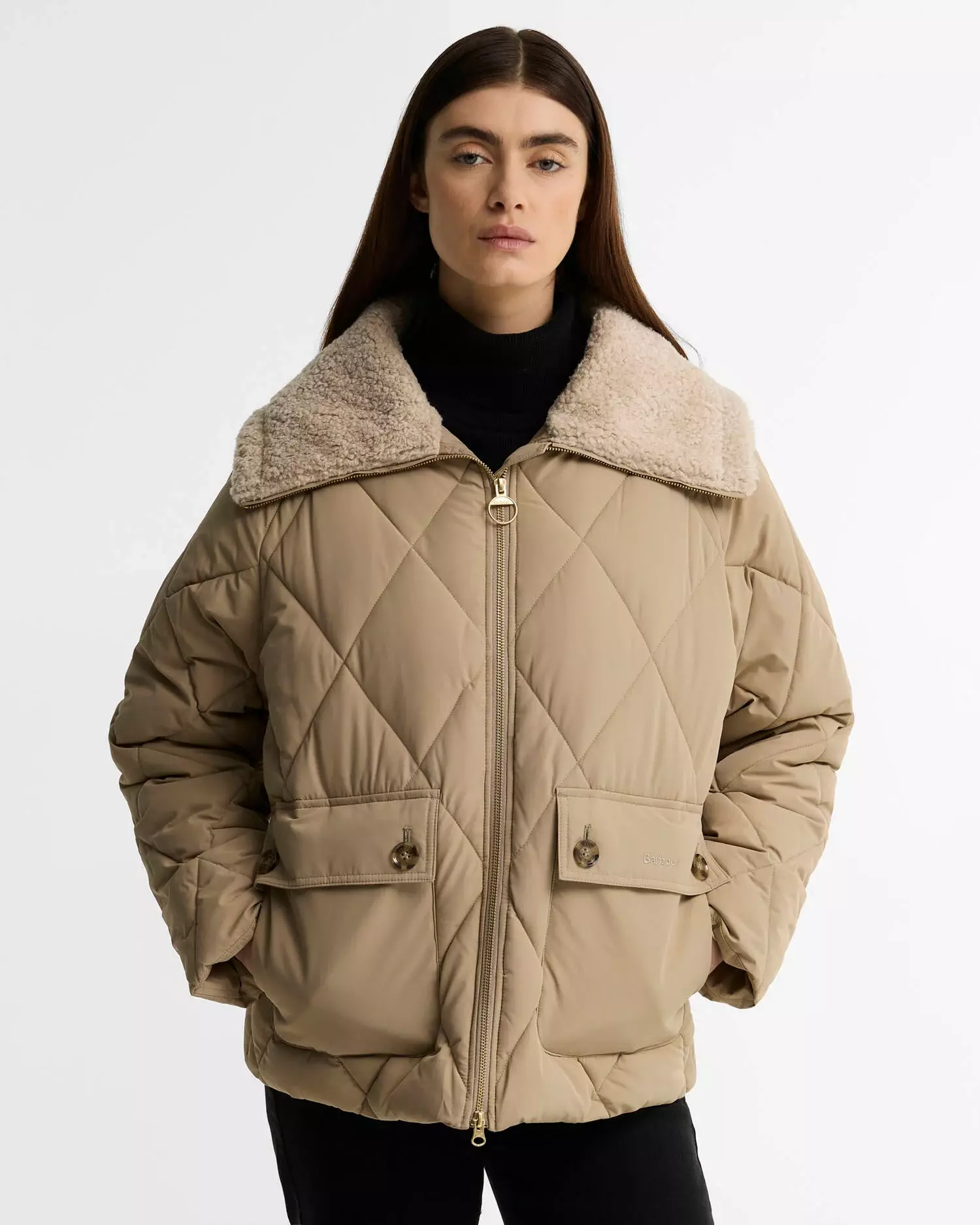 Woman wearing a stylish beige diamond quilted Barbour jacket with a cream faux shearling collar, hands in pockets